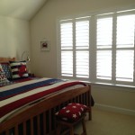 A bedroom with windows that have plantation shutters from A Shade Above Millville DE