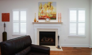Fireplace with painting above it two windows with custom shutters