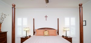 View of bedroom with tall bed posts showing windows with custom shutters